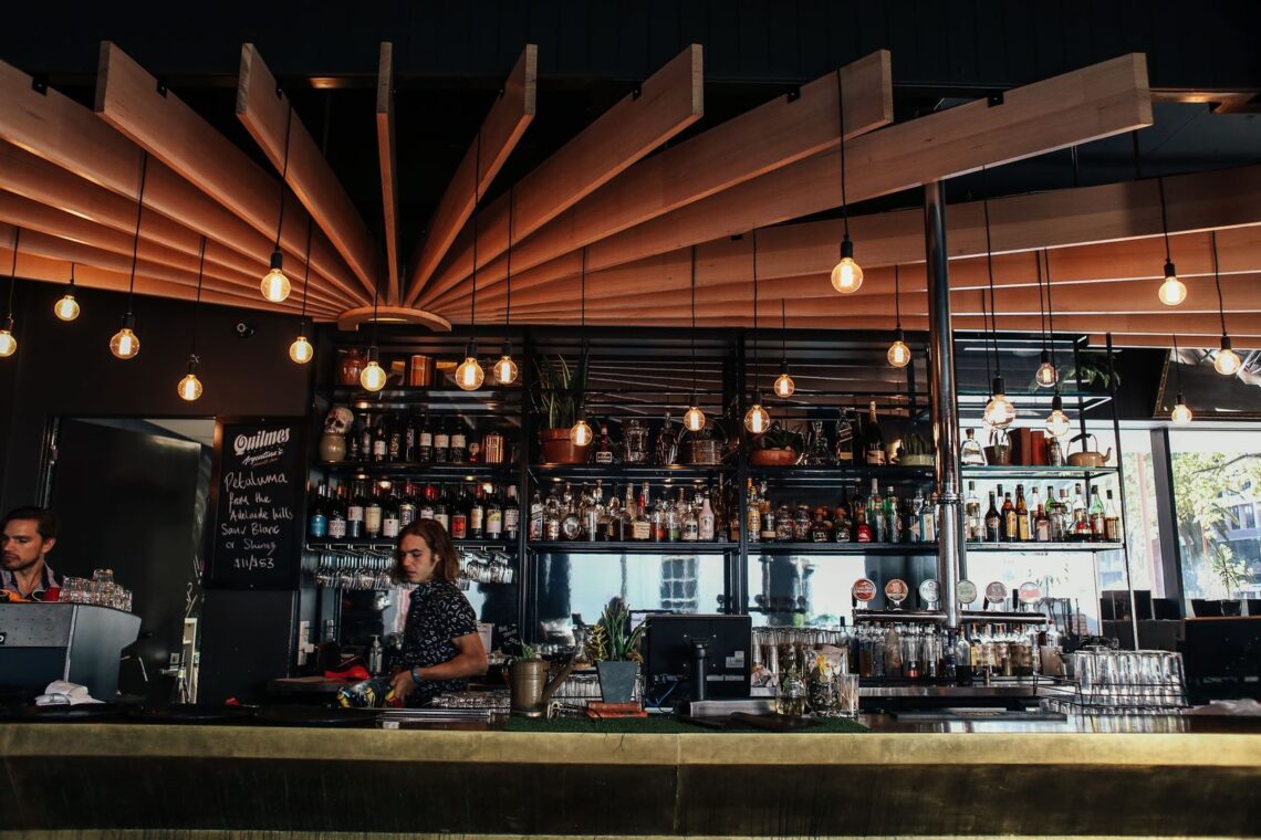 A modern cocktail bar interior with wooden ceiling panels and hanging bulbs