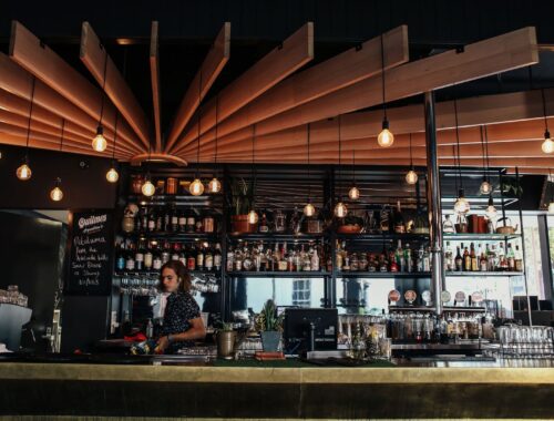 A modern cocktail bar interior with wooden ceiling panels and hanging bulbs