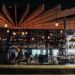 A modern cocktail bar interior with wooden ceiling panels and hanging bulbs